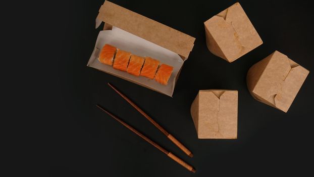 Asian food delivery. Packaging for sushi and woks. Food in paper containers on black background. Open package with salmon rolls