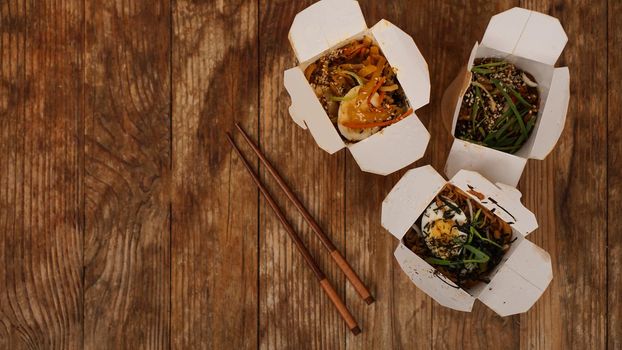 Noodles with pork and vegetables in take-out box on wooden table. Asian food delivery. Food in paper containers on wooden background