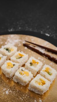 Sushi delivery. Sweet rolls made from rice, pineapple, kiwi and mango. Rolls on a gold and black background. Wooden sticks for sushi.