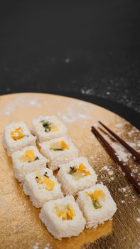 Sushi delivery. Sweet rolls made from rice, pineapple, kiwi and mango. Rolls on a gold and black background. Wooden sticks for sushi.