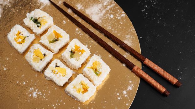 Sushi delivery. Sweet rolls made from rice, pineapple, kiwi and mango. Rolls on a gold and black background. Wooden sticks for sushi.