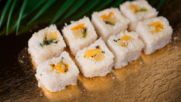 Dessert Sushi - Roll with Various Fruit and Cream Cheese inside. On a gold background and with a tropical leaf