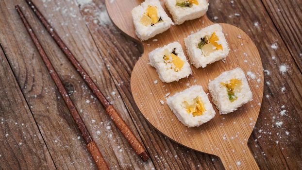 Sushi delivery. Sweet rolls made from rice, pineapple, kiwi and mango. Rolls on a wooden background. Wooden sticks for sushi.