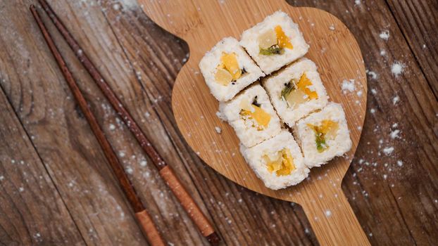 Sushi delivery. Sweet rolls made from rice, pineapple, kiwi and mango. Rolls on a wooden background. Wooden sticks for sushi.