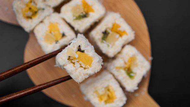 Dessert sushi. Sweet kiwi, pineapple and banana sushi rolls. Sushi on a wooden tray on a black background with a tropical leaf.