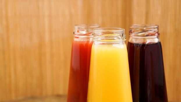 Glass bottles of fresh healthy juice on wooden background. Multi-colored juices. Summer photo and healthy lifestyle, vitamins