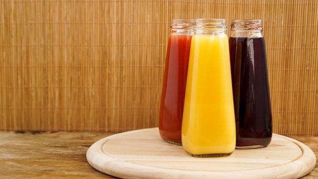 Glass bottles of fresh healthy juice on wooden background. Multi-colored juices. Summer photo and healthy lifestyle, vitamins