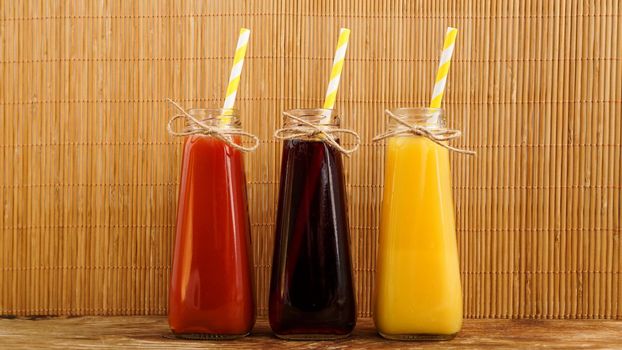 Three multicolored drinks in the bottles on a wooden bamboo background. Bottled paper straws. Full length bottles