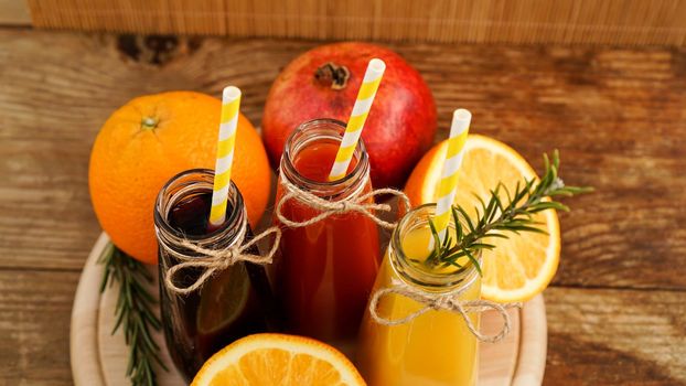 Home made lemonade in little bottles. Multicolored juices and fruits on wooden background. Paper straws in drinks.