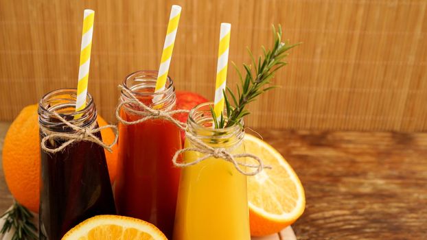 Home made lemonade in little bottles. Multicolored juices and fruits on wooden background. Paper straws in drinks.