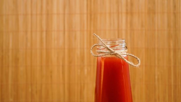 Bottle of tomato juice on wooden background. Bottle neck with twine bow