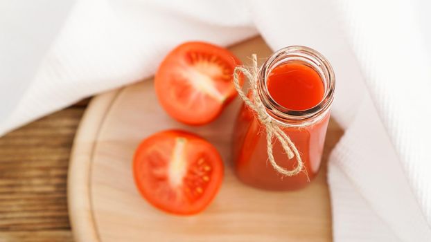 Tomato juice in glass bottle and fresh tomatoes on wooden cutting board and white towel