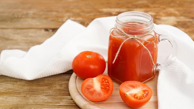 Tomato juice in glass jar and fresh tomatoes on wooden cutting board and white towel