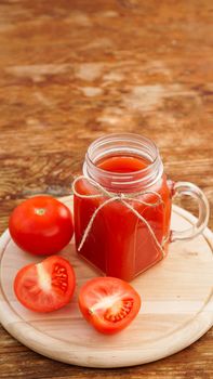 Glass of tomato juice on wooden table. Fresh tomato juice and chopped tomatoes on wooden board. Vertical photo