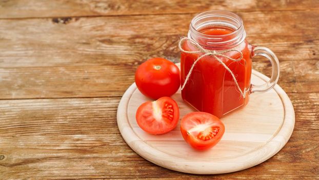 Glass of tomato juice on wooden table. Fresh tomato juice and chopped tomatoes on wooden board