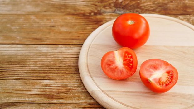 Whole and cut tomato on a wooden board for slicing. Rustic style and wood background. Vegetables and healthy eating. Ingredients for tomato juice