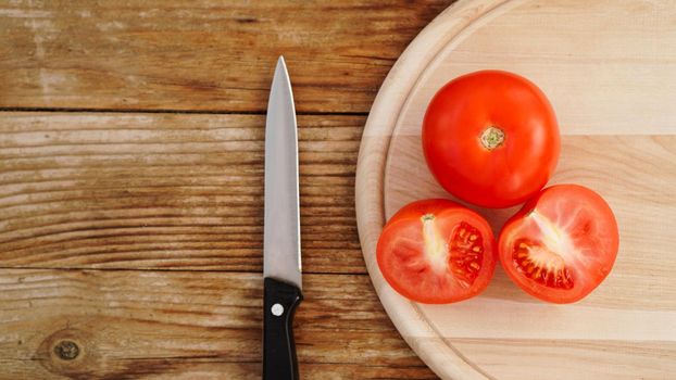 Slice Tomato on a Wooden Cutting Board. Knife and tomatoes on a wooden background. Cooking and kitchen concept