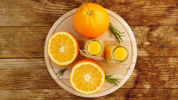 Fresh orange juice on wooden table on a wooden board. Sliced oranges and two bottles of juice. View from above. Rosemary sprigs for decoration