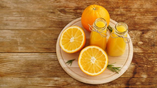 Fresh orange juice on wooden table on a wooden board. Sliced oranges and two bottles of juice. Rosemary sprigs for decoration