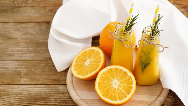 Orange juice in glass bottles. The juice is decorated with a sprig of rosemary. Juice on wooden background with white towel