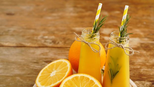 Orange juice in glass bottles. The juice is decorated with a sprig of rosemary. Juice on wooden background