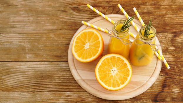 Orange juice in glass bottles. The juice is decorated with a sprig of rosemary. Juice on wooden background