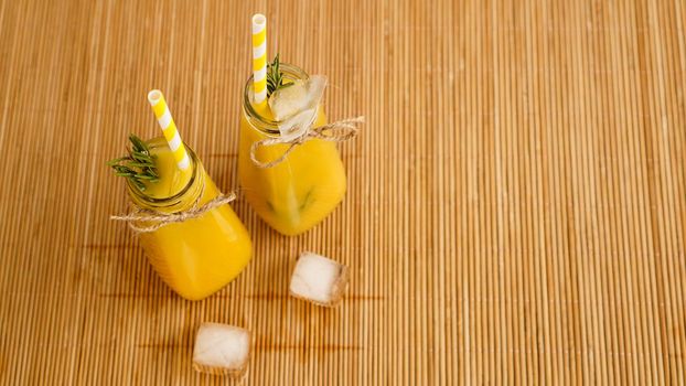 Orange juice bottles and paper straws. Icy drink on a sunny day. Pieces of ice in a bottle and on a bamboo napkin