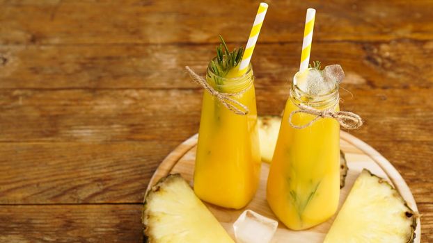 Fresh made Pineapple Juice with Ice in a small glass bottle on wooden background. Homemade drink.