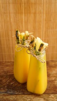 Pineapple juice in a small bottle. Pineapple slices decorate the drink. Juice on wooden background