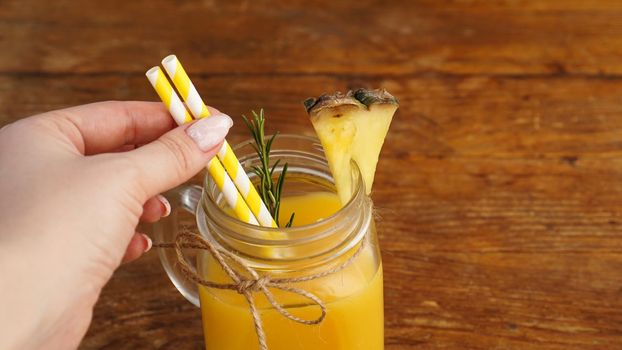 Woman Hand holds a straw, a glass of fresh pineapple juice, close up, healthy lifestyle concept