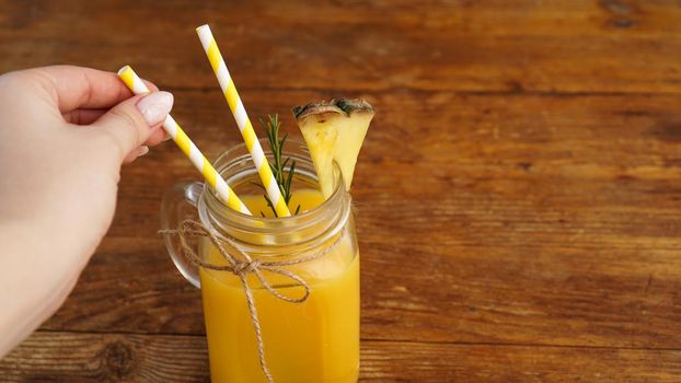 Woman Hand holds a straw, a glass of fresh pineapple juice, close up, healthy lifestyle concept