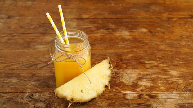 Pineapple juice on a wooden background. A glass jar with juice and a slice of fresh pineapple. Exotic fruits and healthy juice with vitamins