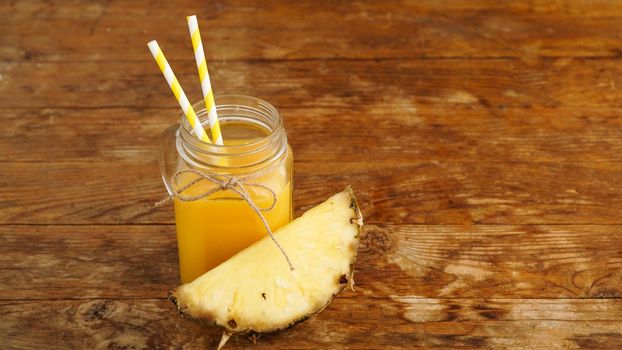 Pineapple juice on a wooden background. A glass jar with juice and a slice of fresh pineapple. Exotic fruits and healthy juice with vitamins