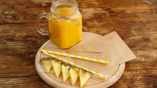 Pineapple juice in a glass jar on a wooden background. Envelope with a letter on a wooden board. Morning note and fruit breakfast