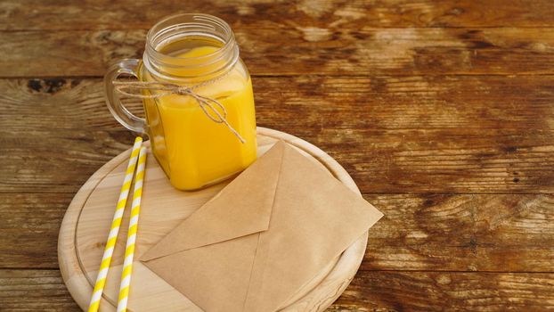 Orange juice in a glass jar on a wooden background. Envelope with a letter on a wooden board. Morning note and fruit breakfast