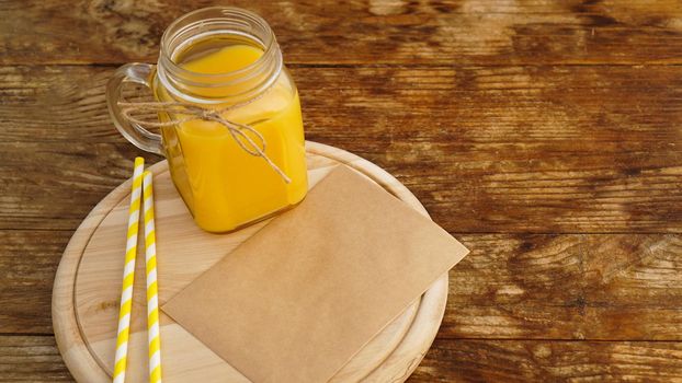 Orange juice in a glass jar on a wooden background. Envelope with a letter on a wooden board. Morning note and fruit breakfast