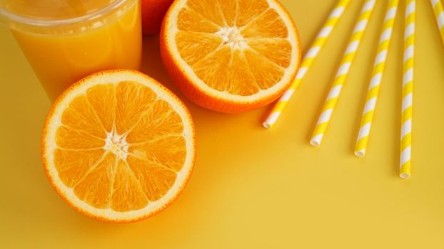 Orange juice in fast food closed cup with tube on yellow background. Sliced orange and yellow paper straws for a drink