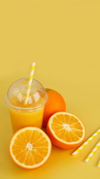 Orange juice in fast food closed cup with tube on yellow background. Sliced orange and yellow paper straws for a drink. Vertical photo