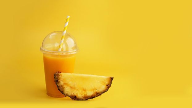 Pineapple juice in a plastic cup on yellow background. Tropical juice - summer banner