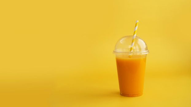 A plastic cup of orange drink. Natural juice or smoothies. Healthy food. Vegetarian or vegan food on yellow background