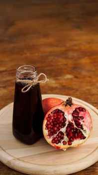 Ripe pomegranates with juice on wooden background. Red juice in small glass bottle on wooden background. Vertical photo