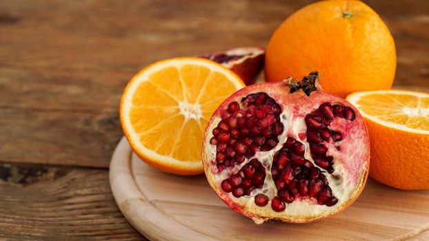 Pomegranate and oranges on a wooden background. Cut fruit. The concept of healthy food and vitamins.