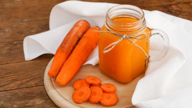 Bright orange carrot juice in a glass jar on a wooden background. Juice and chopped carrots. Homemade drink with vitamins