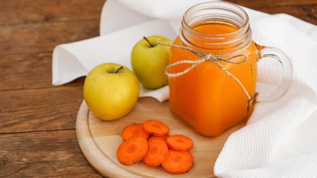 Apple and carrot juice in glass, fresh vegetables and fruits on wooden background. Rustic style. Homemade drink with vitamins