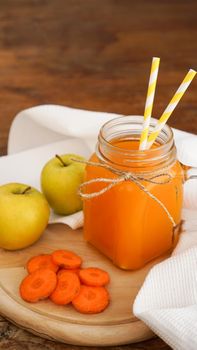 Apple and carrot juice in glass, fresh vegetables and fruits on wooden background. Rustic style. Homemade drink with vitamins. Vertical photo