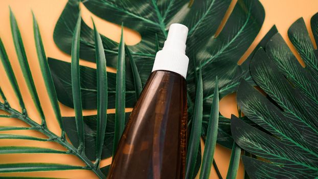 Suntan lotion bottle on soft orange background with tropical leaf. Top view, copy space. Sun protection cosmetic products, summer skin care concept