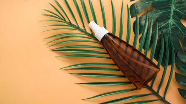 Suntan lotion bottle on soft orange background with tropical leaf. Top view, copy space. Sun protection cosmetic products, summer skin care concept