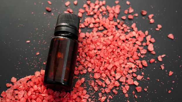 Beautiful spa composition with vial and red sea salt for bath on black background.