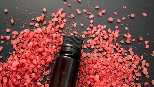 Beautiful spa composition with vial and red sea salt for bath on black background.