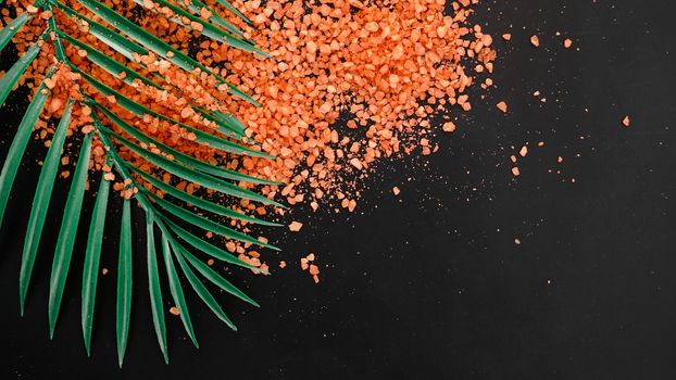 Orange sea salt on a black background. Tropical palm leaves on background. Beauty concept. Spa background with a space for a text